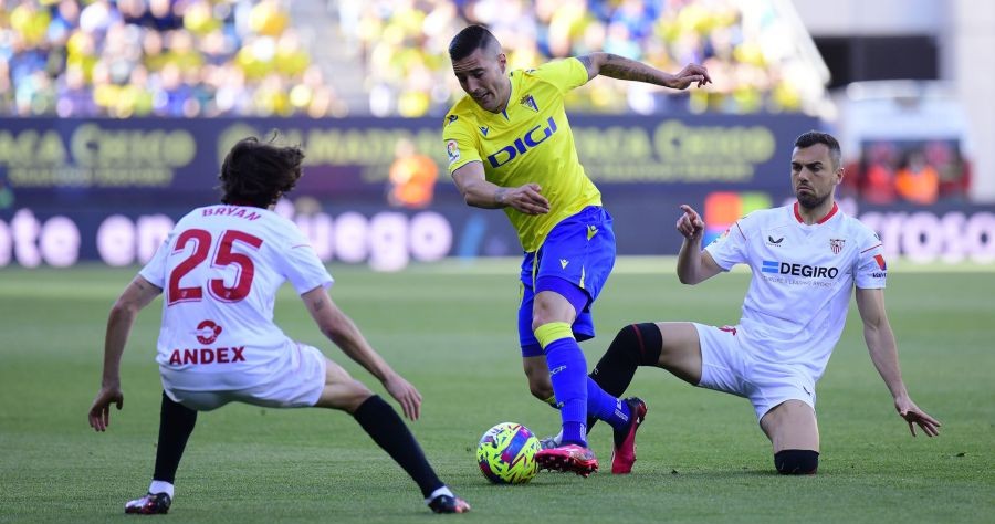 Sergi Guardiola pasa entre dos jugadores del Sevilla en el Nuevo Mirandilla